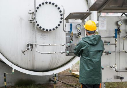 A worker in safety gear operates a large industrial machine outdoors, ensuring operational safety.